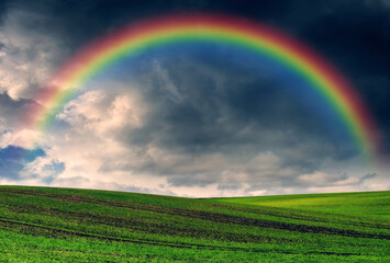 Scenic view of rainbow over green field. dramatic gray sky over a picturesque hilly field