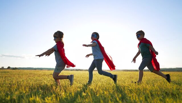 Happy family. Children dressed as superheroes play in the park. Superhero teamwork. Strong children dream of victory. Children are superheroes winners. Family game in nature. Superheroes in red capes