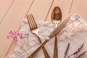 Cutlery, napkin and floral decor on color wooden background