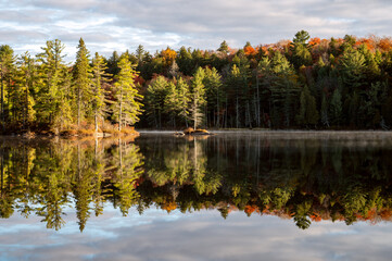 Islands and trees reflecting with clouds on a calm lake in the morning. Pincher Lake, Algonquin Provincial Park, Ontario, Canada.
