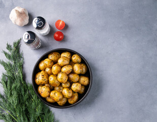 Young roasted baby potatoes in a black  pan with tomatoes, garlic and herb on a blue background.