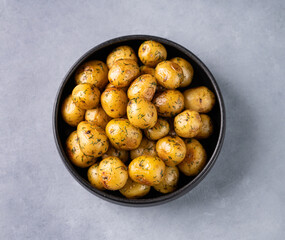 Young roasted baby potatoes in a black  pan on a blue background.