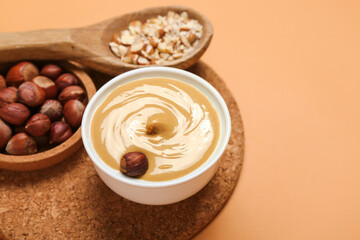 Bowls of tasty nut butter and hazelnuts on color background, closeup