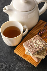Wooden board with sesame halva, cup of tea and teapot on dark background, closeup