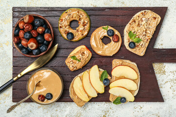 Wooden board of delicious sandwiches with nut butter, apples, hazelnuts and blueberry on light background, closeup