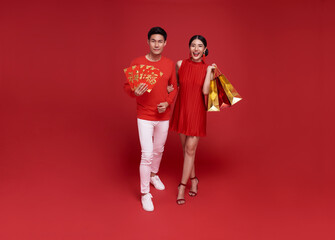 Happy Asian couple holding shopping bags and red envelopes isolated on red background for Chinese...