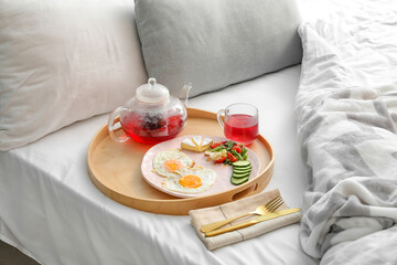 Wooden tray with tasty breakfast on comfortable bed