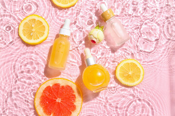 Bottles of vitamin C serum in water on pink background