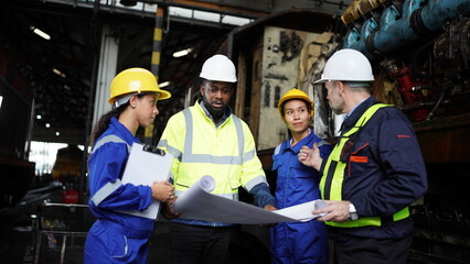 Engineers in discussion in machine maintenance in factory. Group of Industrial Engineers with Blueprint against trains and machinaries industry background. Studying Blueprint with Superior