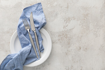 Table setting with blue napkin and cutlery in plate on light background