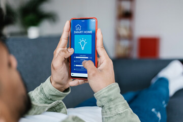 Young adult man using IOT automation app on smart phone dimming the house lights - Technology and innovation concept