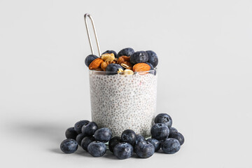 Glass of chia pudding with blueberries, nuts and oat flakes on light background