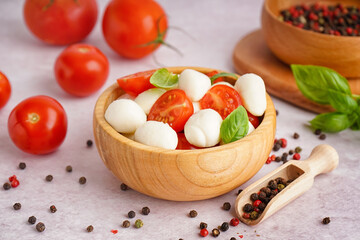 Wooden bowl with tasty mozzarella cheese, tomatoes and spices on light background
