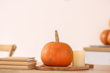 Board with fresh pumpkin, burning candles and books on counter in kitchen