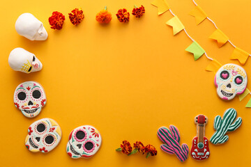 Frame made of cookies, skulls, flags and flowers on orange background. El Dia de Muertos