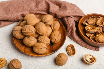 Plate with fresh walnuts on light background