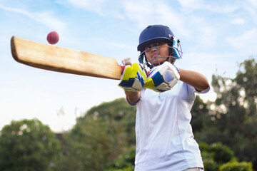 Female cricket player wearing protective gear and hitting the ball with a bat on the field