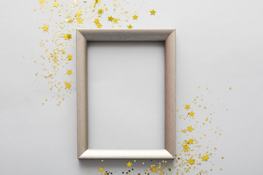 Composition with empty picture frame and golden sequins on grey background