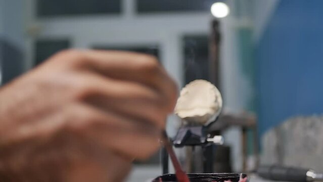 Detailed. The hands of an orthodontist dental technician make a denture by working with molten liquid paraffin waxing artificial gums using a hot metal plate