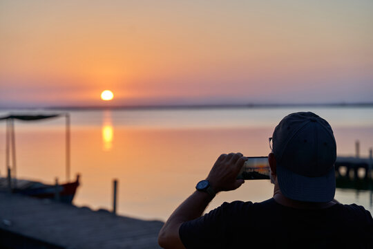 Tourist taking picture of sunset in Albufera lake dock in Valencia