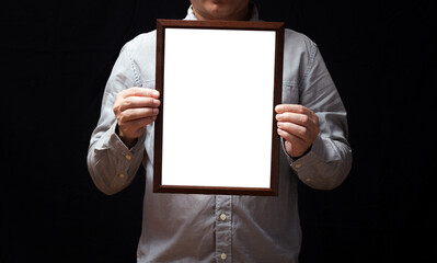 A blank diploma or a mockup certificate in the hand of a man employee wearing shirt on black background. The vertical picture frame is empty and the copy space.