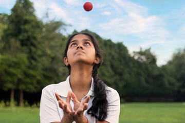 Girl wearing cricket uniform catching the ball on the field