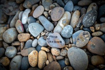 Shallow focus of wishing stones and pebbles seen on a beach. Hand written Piece in Ukraine is written on a large pebble.