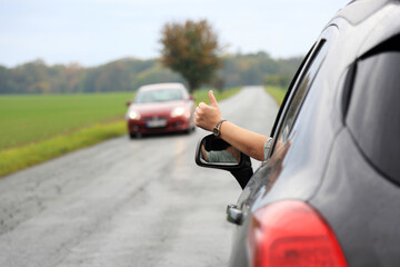 Dłoń kobiety, ręka wysunięta przez okno samochodu osobowego, suwa, na drodze przez pola.