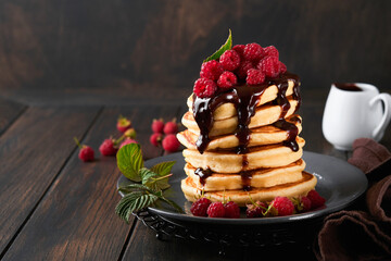 Pancakes. Pancakes with fresh raspberry with chocolate glaze or toppings in gray bowl on old wooden table background. Homemade classic american pancakes. Page for magazine concept.