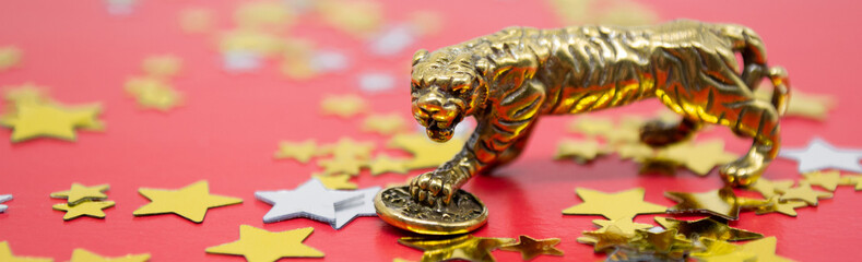 Banner with a bronze figure of a tiger with a coin on a red background and golden stars, copy space