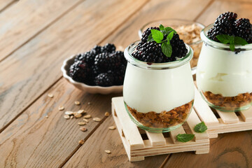 Yogurt with granola, blackberry berry fruits and muesli served in glass jar on wooden background. Healthy breakfast concept. Healthy food for breakfast, top view