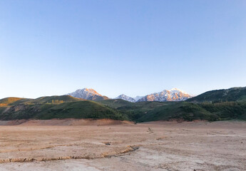 Landscape with mountains, snoe peaks and green hills. Dry cracked earth. Drought. The dried-up bottom of the river