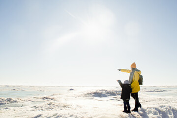 Faceless woman in yellow raincoat and child standing and looking on frozen sea
