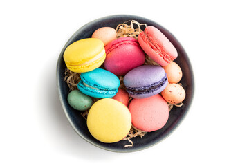 Different colors macaroons and chocolate eggs in blue ceramic bowl isolated on white background. top view, close up.