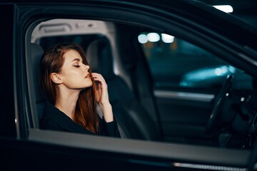 a stylish, luxurious woman is sitting in a black car at night, straightening her long, styled hair, closing her eyes with pleasure