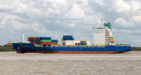 Obraz premium A container ship loaded with containers sails alongside the shore