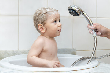 A little boy sits in the sink and fearfully looks at the shower