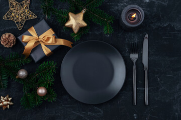 Stylish table setting, gift box, fir branches, star and balls with black plate, cutlery and candle...