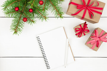 Christmas composition. Notepad, gifts and fir tree branches with red ornaments on white wooden background.