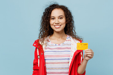 Young happy woman of African American ethnicity 20s she wear red jacket hold in hand mock up of credit bank card isolated on plain pastel light blue cyan background. Wet fall weather season concept.