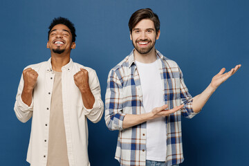 Young two friends fun men wear white casual shirts together point index finger aside indicate on area mock up do winner gesture isolated plain dark royal navy blue background People lifestyle concept - obrazy, fototapety, plakaty
