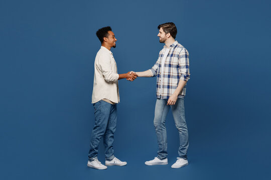 Full Body Young Side View Two Friends Fun Men Wear White Casual Shirts Looking Camera Together Shaking Hands Meeting Each Other Isolated Plain Dark Royal Navy Blue Background People Lifestyle Concept