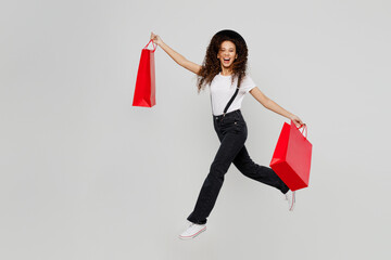 Full body side view jubilant happy young woman wear t-shirt hat hold in hand red paper package bags...