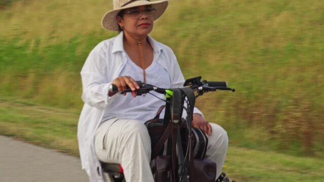 Woman with a disability in the wheelchair mobility scooter enjoying summer park in the evening. Carefree woman with mobility issue uses electric three wheel wheelchair scooter having fun.