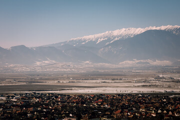 Panoramic view over the ski slope Poiana Brasov ski resort in Transylvania, Pine forest covered in snow on winter season,Mountain landscape in winter with the Bucegi Mountains in the background.