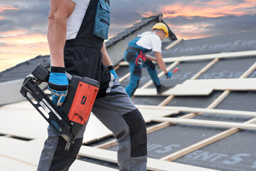 The electric nail gun in a worker hand while working on the roof. - obrazy, fototapety, plakaty
