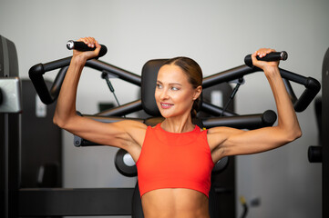 Athletic woman trains shoulders on a machine in gym