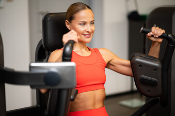 Naklejka na ściany i meble Woman using a chest press machine in a gym