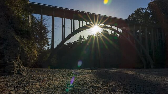 Sunburst sunrise behind highway bridge from a sandy beach - timelapse