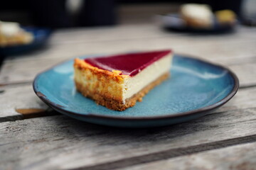 piece of cheesecake with a raspberry fruit glaze on a blue plate on a wooden tabel. 